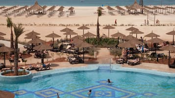 Un resort con piscina, sillas de descanso, sombrillas y una playa al fondo.