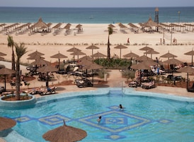 Un resort con piscina, sillas de descanso, sombrillas y una playa al fondo.