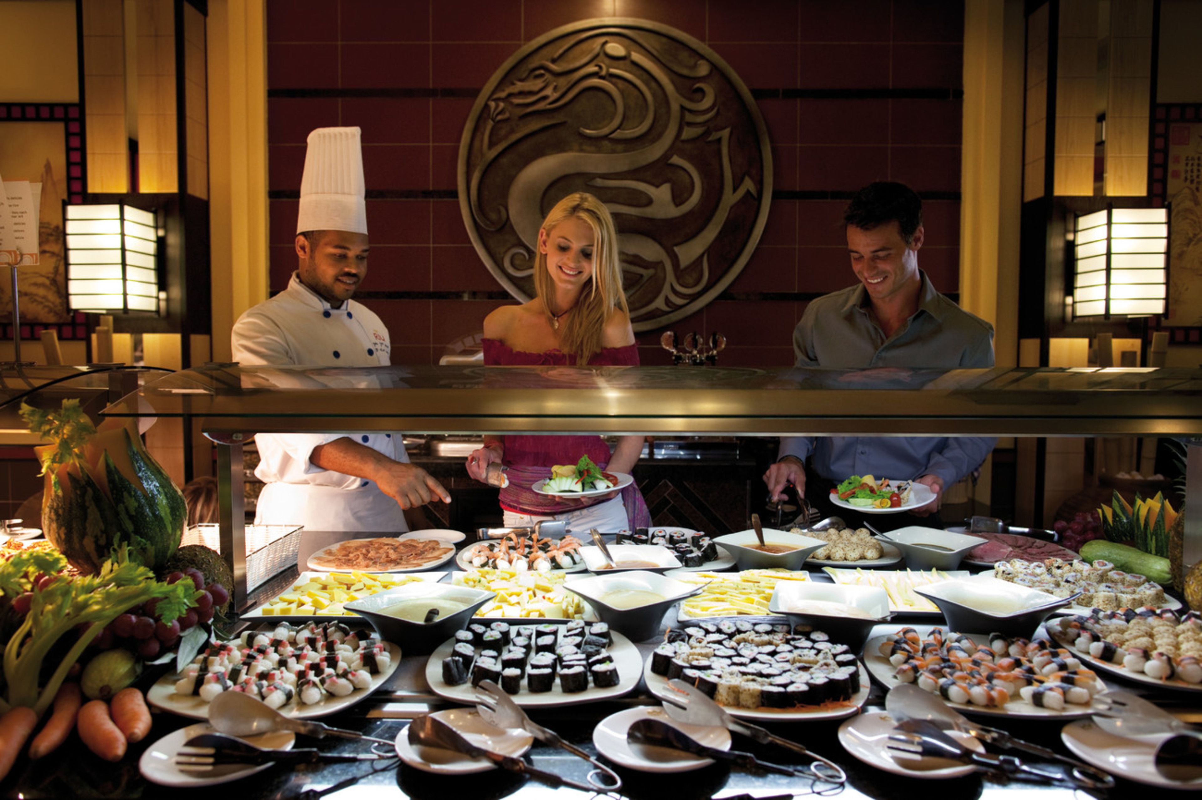 A buffet with various dishes and a decorative wall with a dragon design.