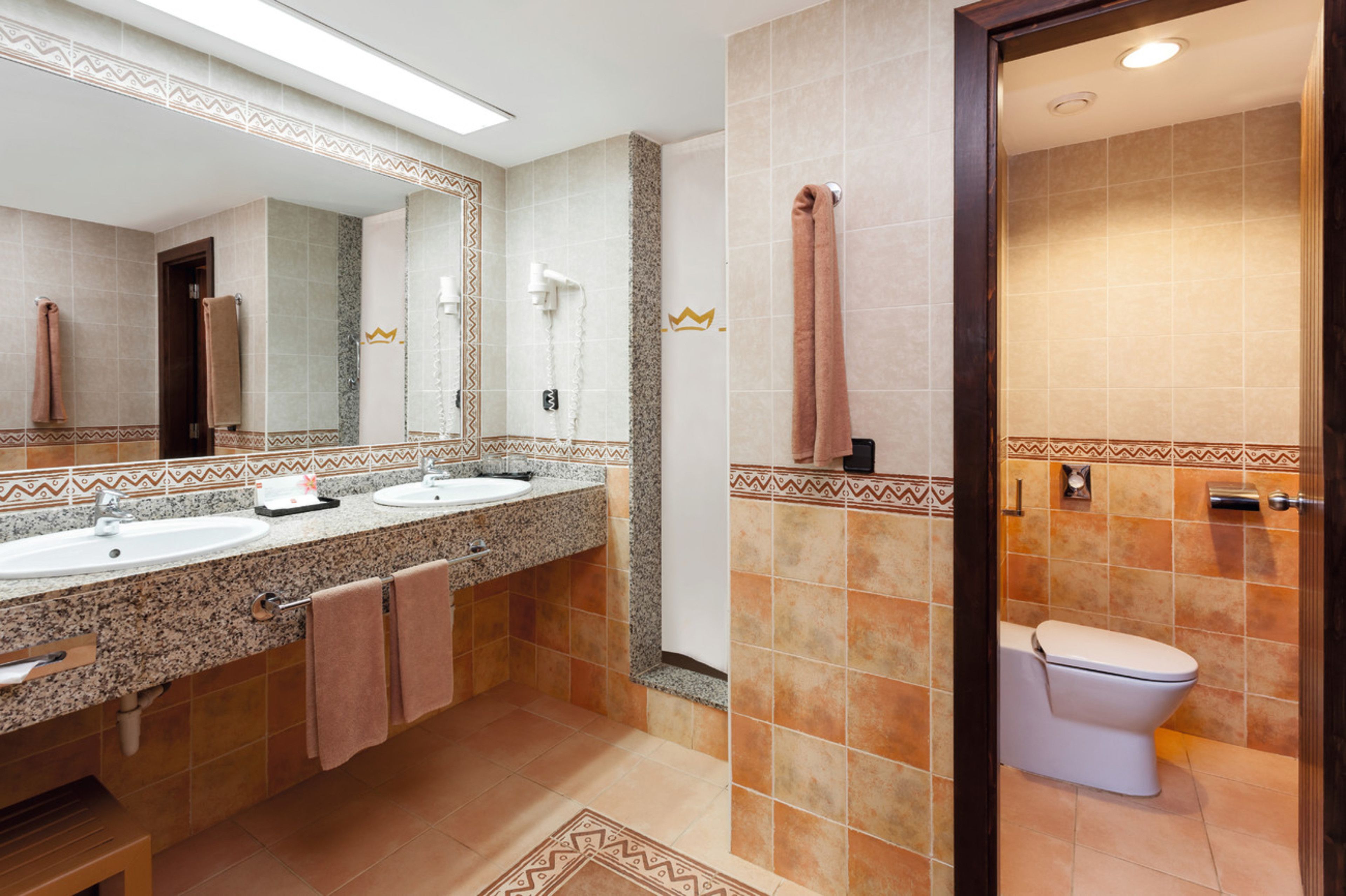 Un baño con dos lavamanos, un espejo, un inodoro y un perchero para toallas.