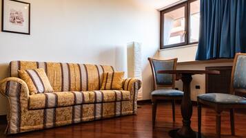 A living room with a patterned sofa, two chairs, a wooden table, and a window with curtains.