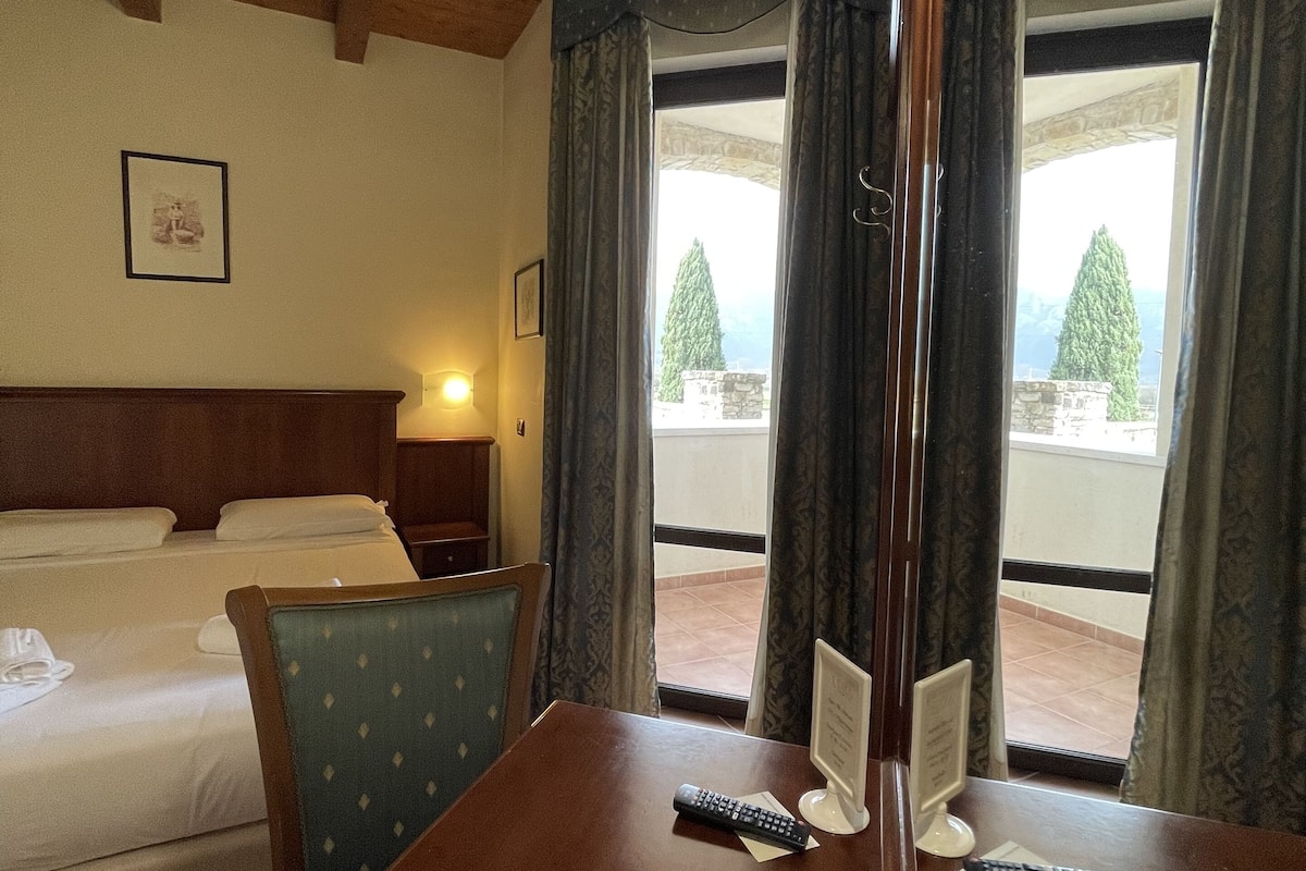 A hotel room with a bed, a table with a remote control, and a window with curtains.