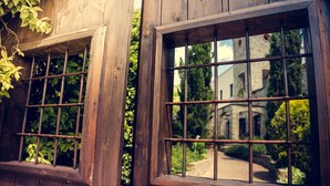 A wooden building with barred windows and a stone pathway leading to a white building in the background. - Hotel Villa Venus (Atena Lucana)