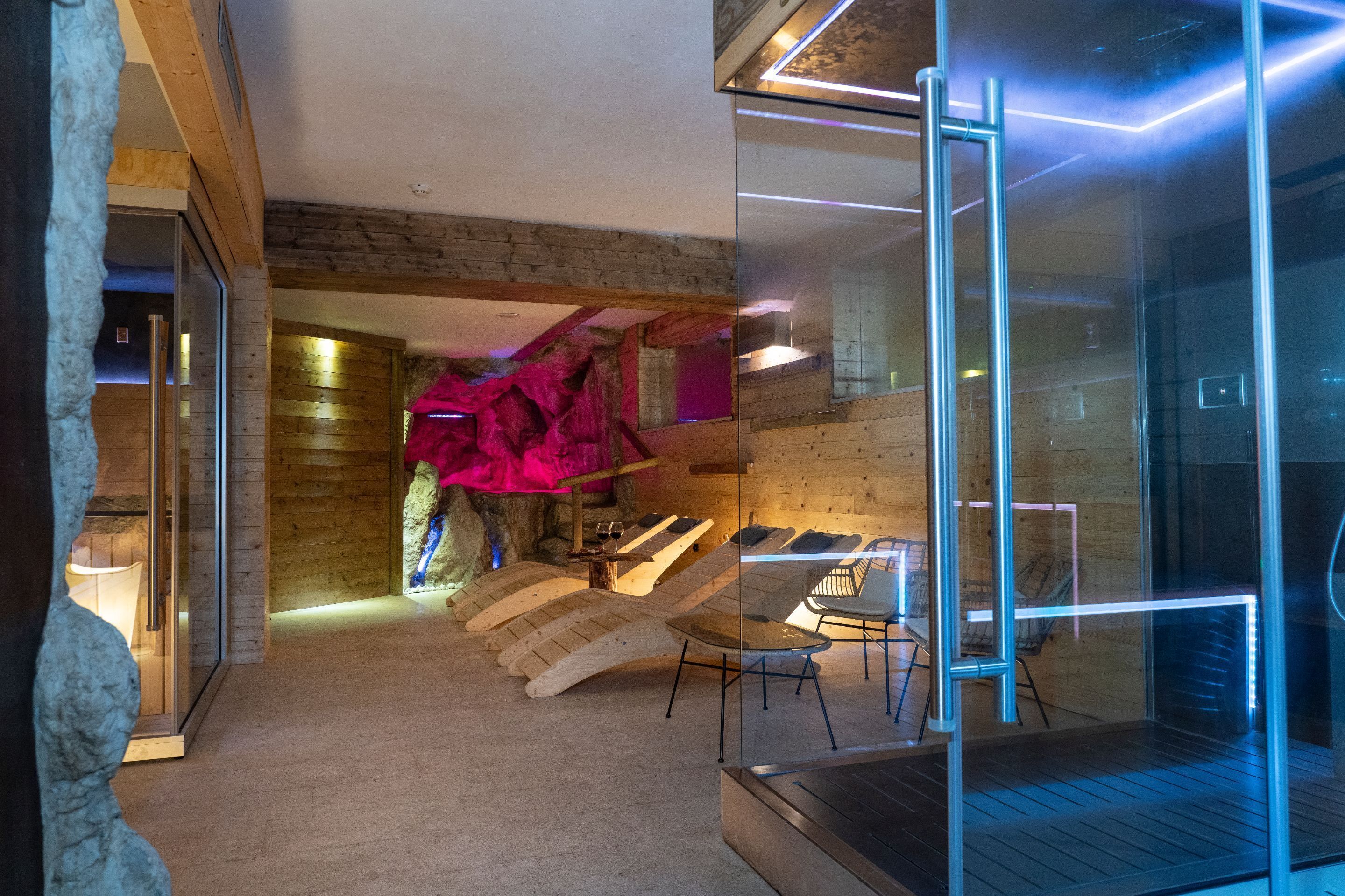 A modern spa area with wooden walls, a glass enclosure, and a relaxation area with chairs.
