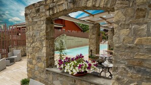 A stone archway leading to a pool area with outdoor seating and a view of a building with a red roof. - Hotel Villa Venus (Atena Lucana)