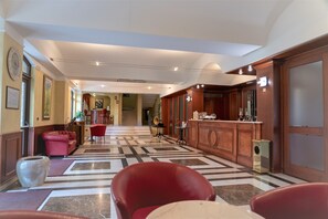 A hotel lobby with a check-in counter, red seating, and a marble floor. - Hotel Villa Venus (Atena Lucana)