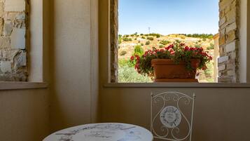 Una habitación con vista a una colina, una mesa con mantel temático de vino y una silla con respaldo decorativo.