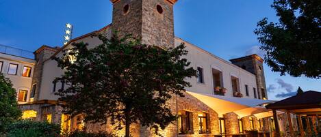 A historic building with a stone tower, arched windows, and a covered patio area.