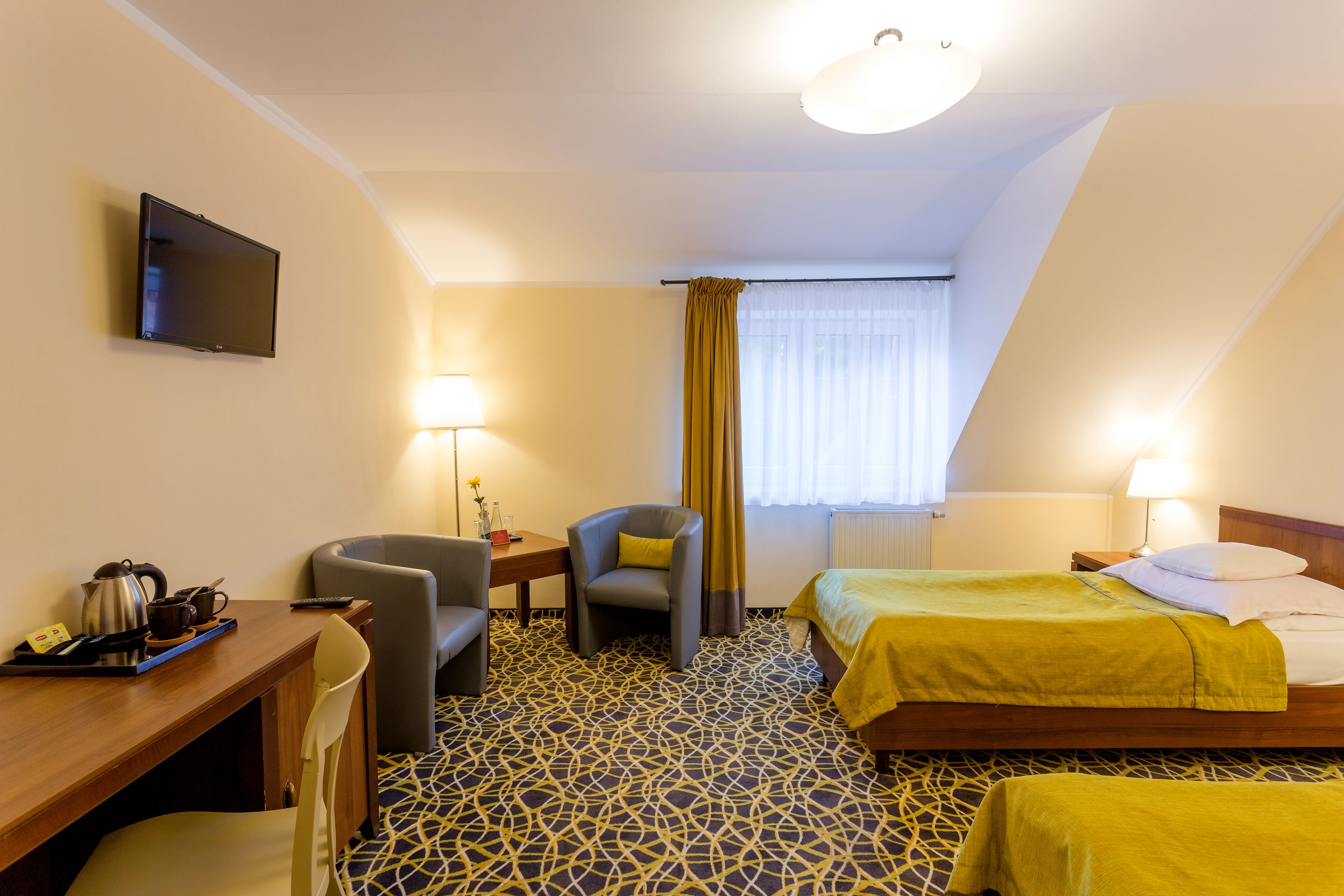 A hotel room with a bed, a desk, a chair, a TV, and a window with curtains.