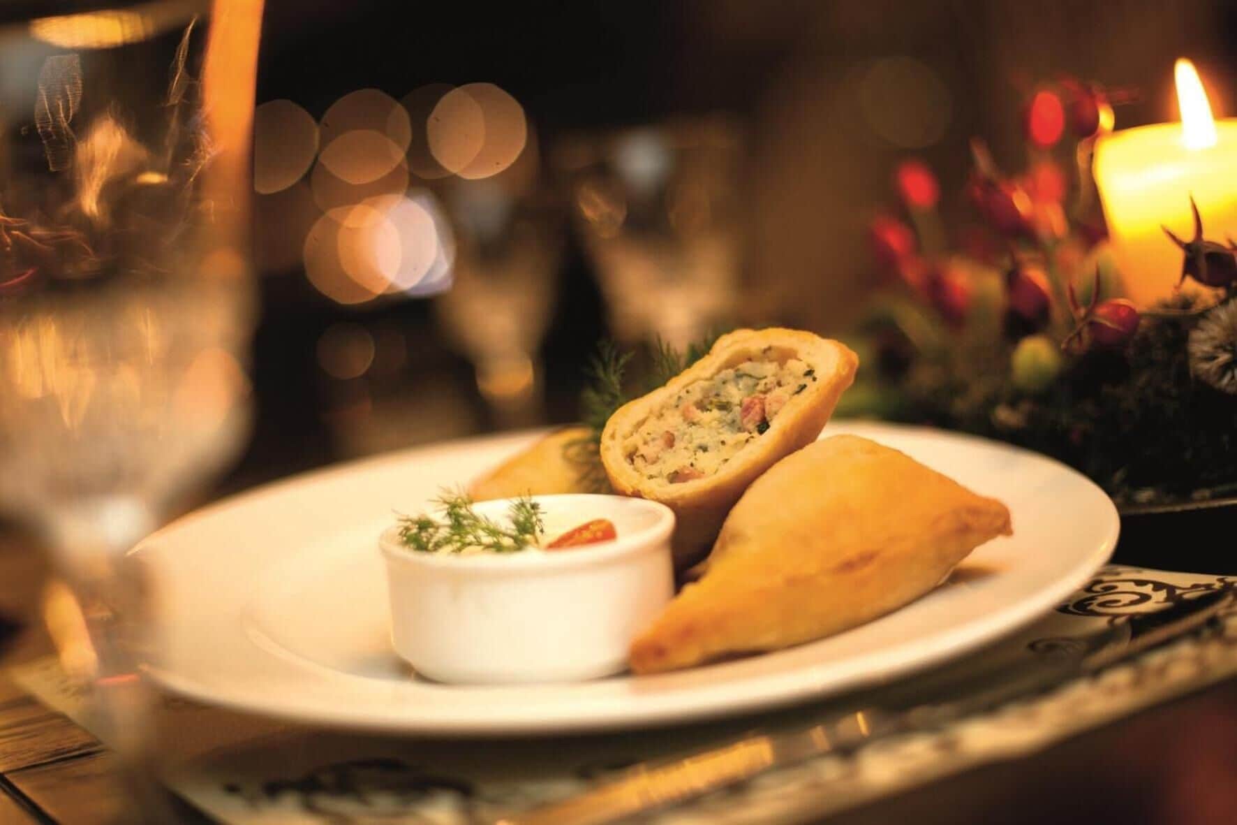 A plate with a stuffed pastry and a small bowl of sauce, set on a table with a candle and decorative elements.