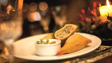A plate with a stuffed pastry and a small bowl of sauce, set on a table with a candle and decorative elements.