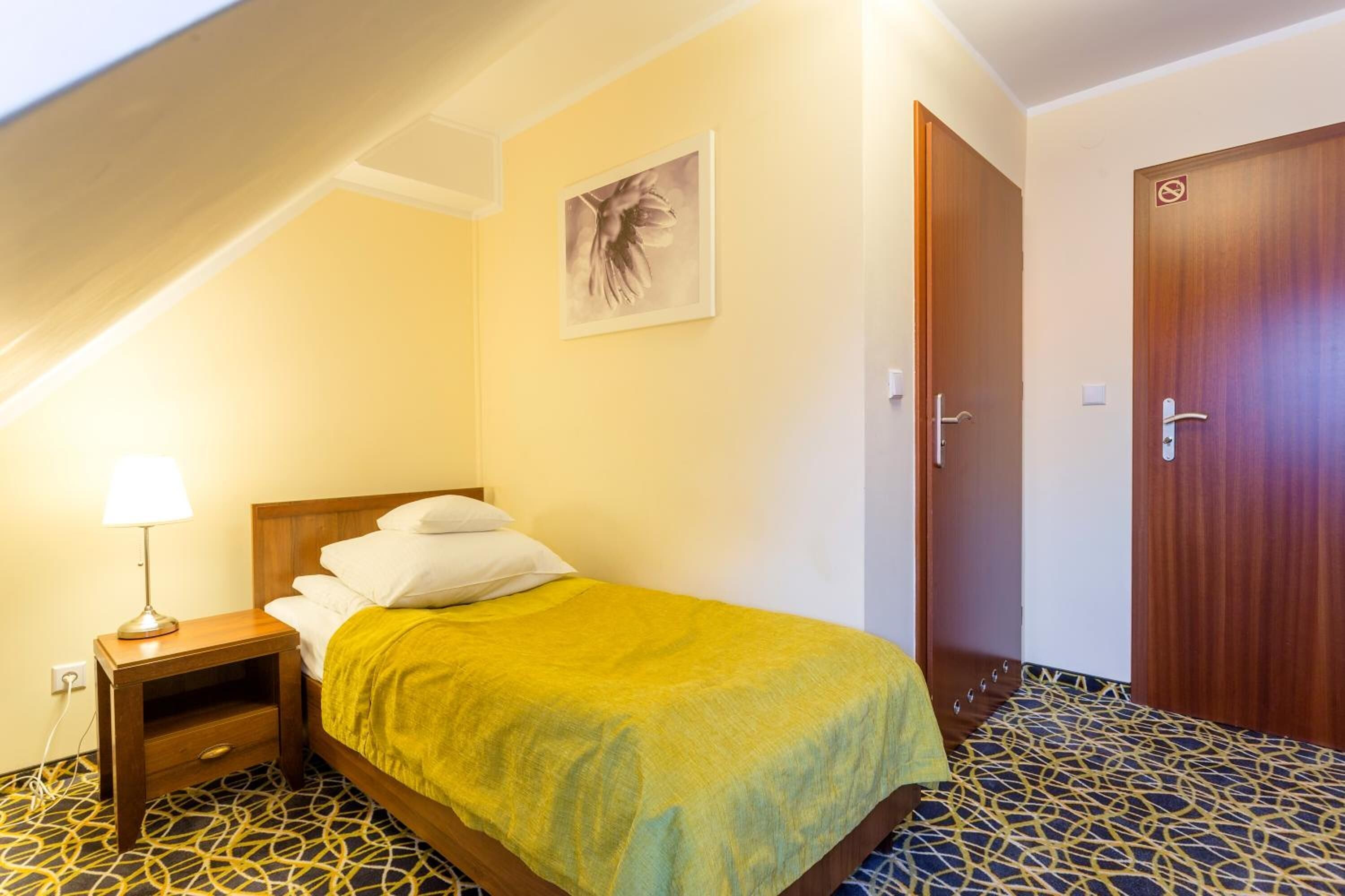 Un dormitorio con una cama, una mesita de noche con lámpara, una puerta y un cuadro colgado en la pared.