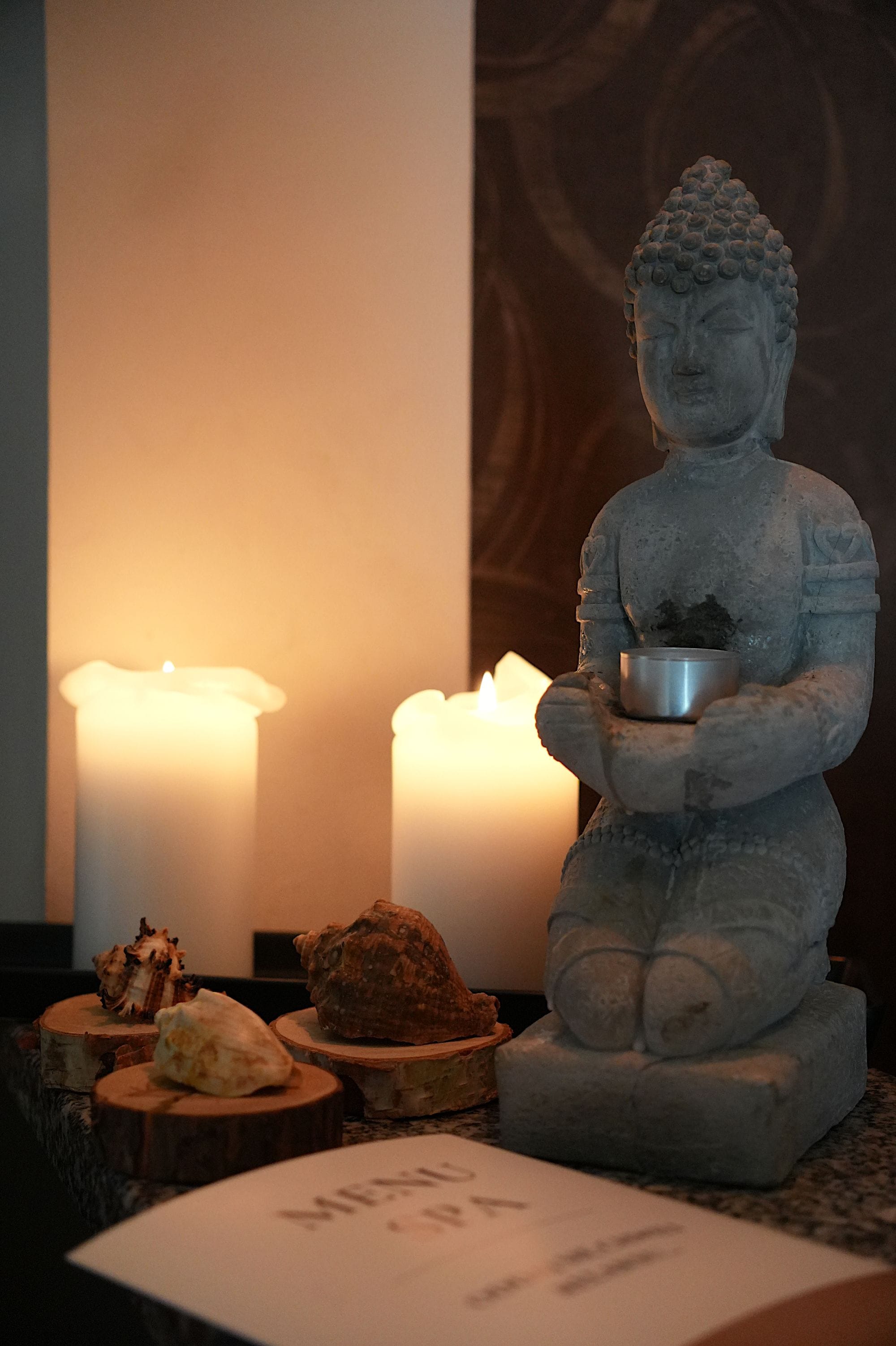 A statue of a seated figure holding a bowl, surrounded by candles and decorative items on a table.