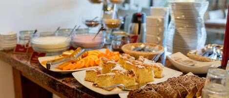A buffet with various dishes including cakes, fruits, and beverages.
