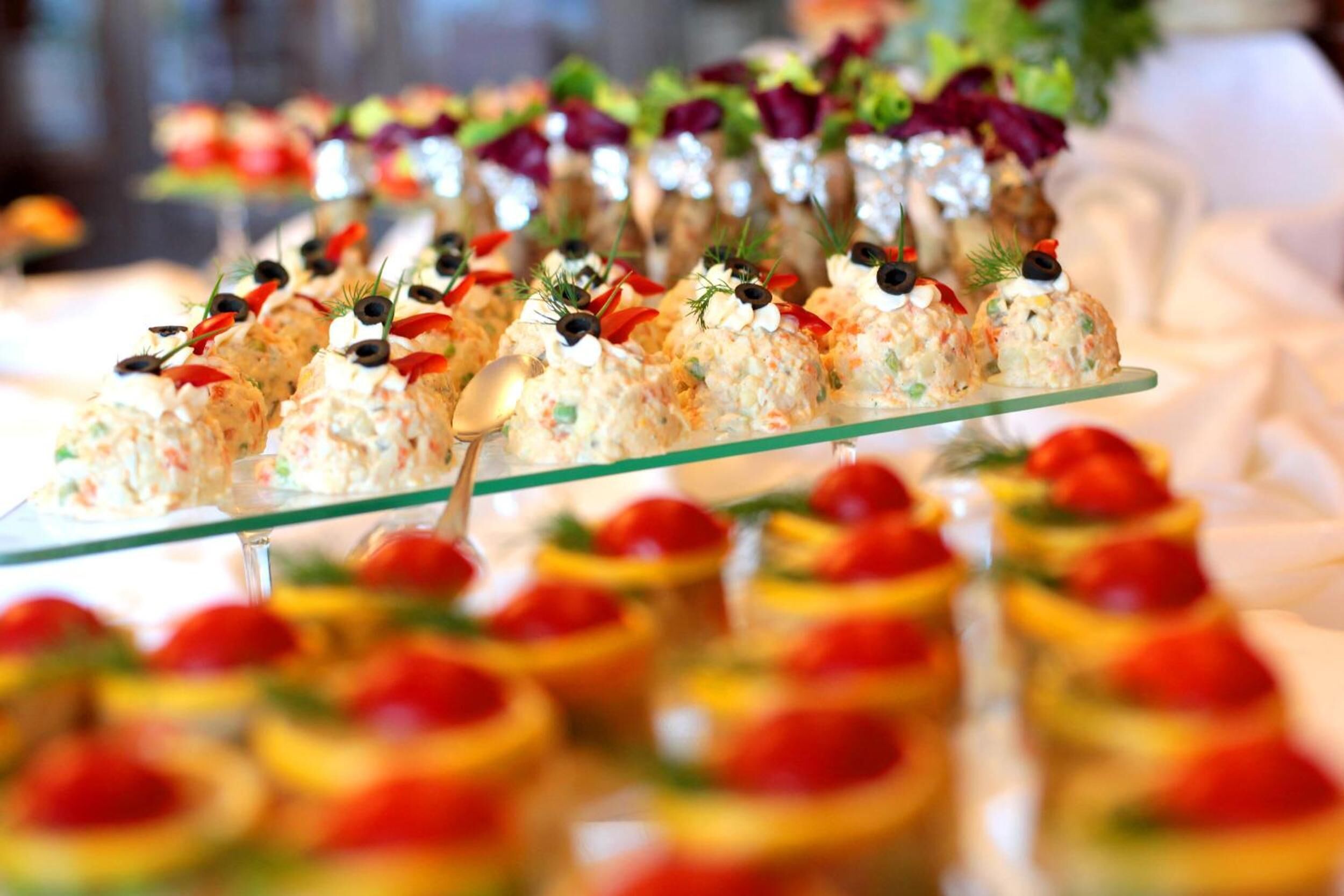 Un buffet proposant une variété de plats, notamment un plat en verre accompagné d’une cuillère et une assiette en verre contenant de la nourriture décorée d’herbes et d’olives.