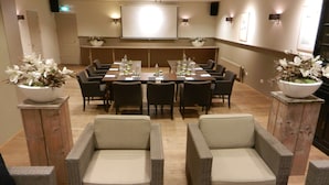 A conference room with a long table, chairs, and a projector screen. There are two side tables with flower arrangements. - De Klomp - Charme Hotel & Restaurant (Vilsteren)