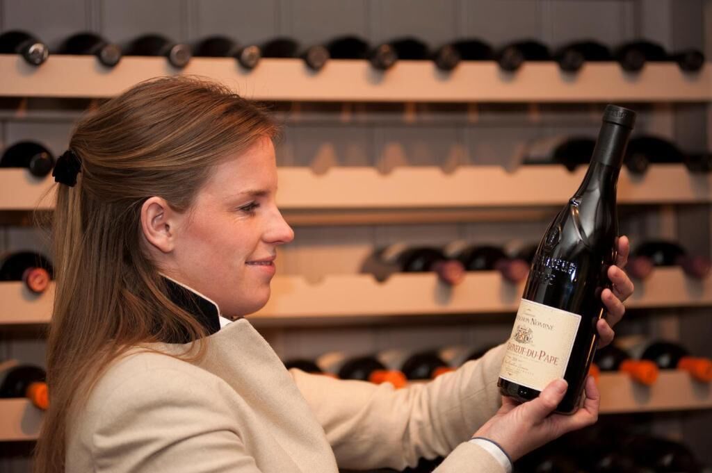 Une personne tenant une bouteille de vin dans une cave à vin, avec des étagères remplies de bouteilles de vin en arrière-plan.