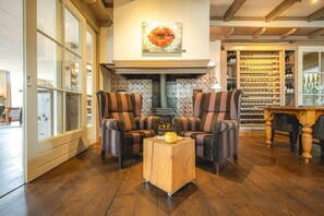 A room with two striped armchairs, a small wooden coffee table, a fireplace, and a wine rack. - De Klomp - Charme Hotel & Restaurant (Vilsteren)
