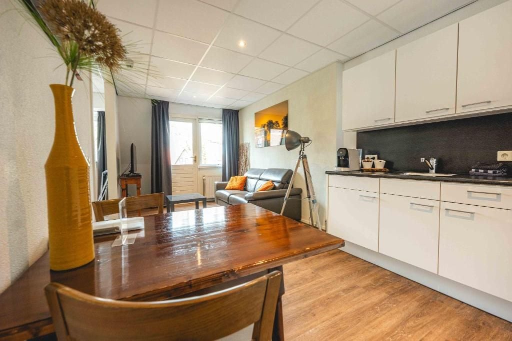 A modern kitchen with white cabinets, a dining table with chairs, and a large vase with dried plants.