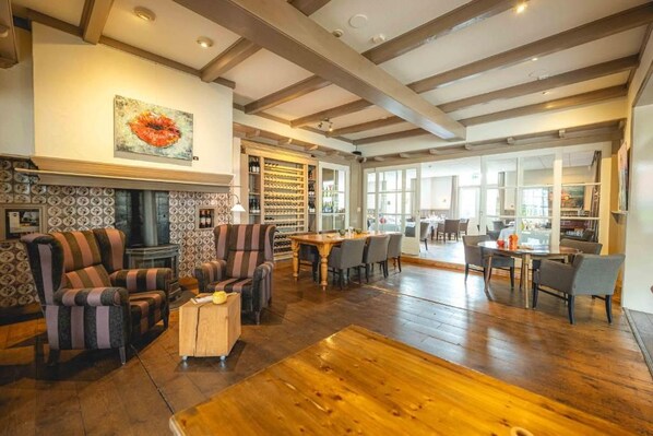 A spacious living area with a fireplace, patterned wallpaper, and a wine rack. - De Klomp - Charme Hotel & Restaurant (Vilsteren)