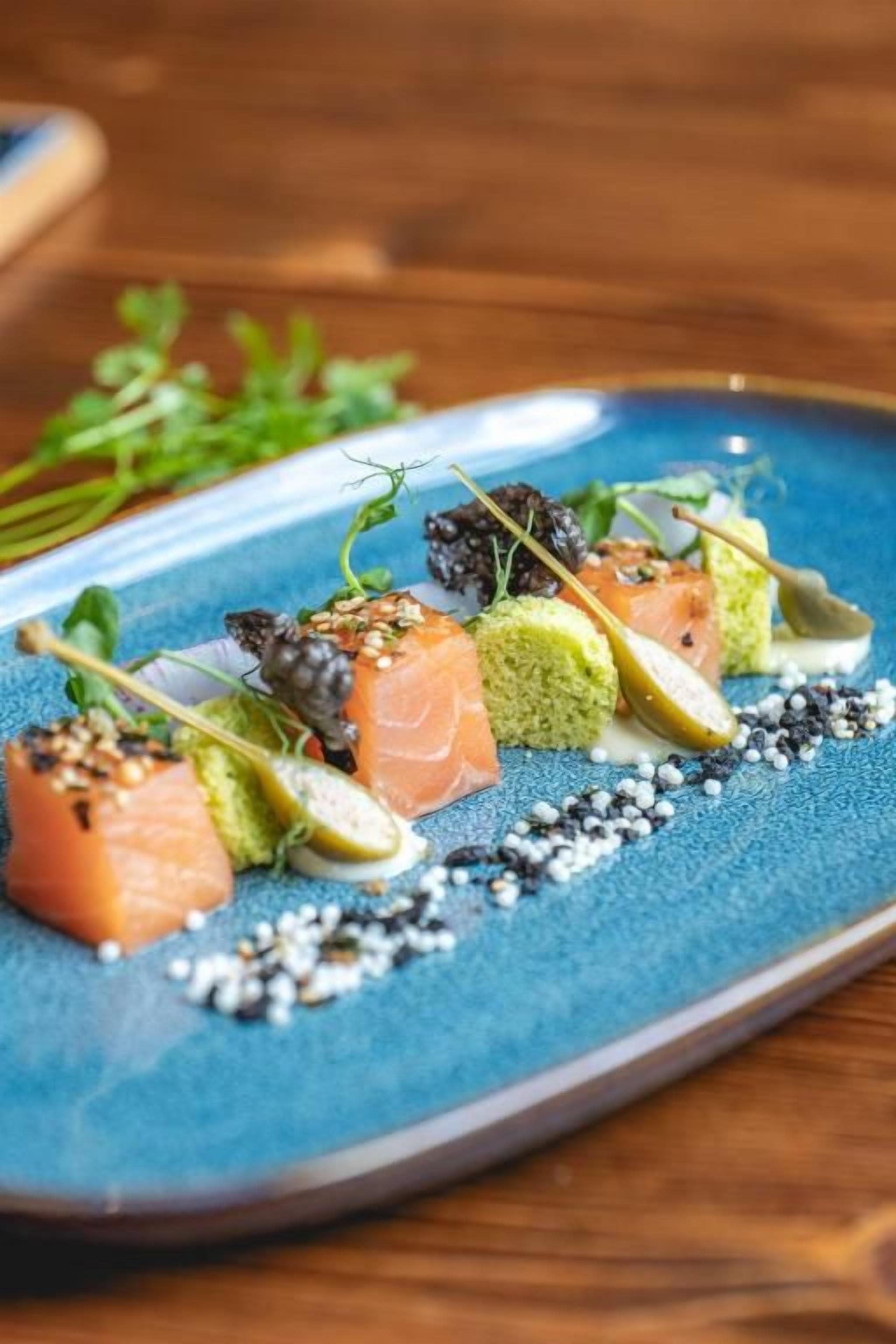 Un plato azul con alimentos, como salmón y verduras, sobre una mesa de madera.