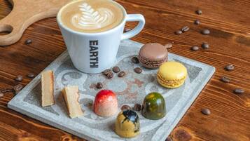 A white mug with 'EARTH COFFEE' text, a cup of coffee with latte art, and assorted macarons on a wooden table.