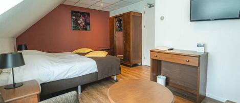 Un dormitorio con cama, mesita de noche, lámpara y televisor en la pared.