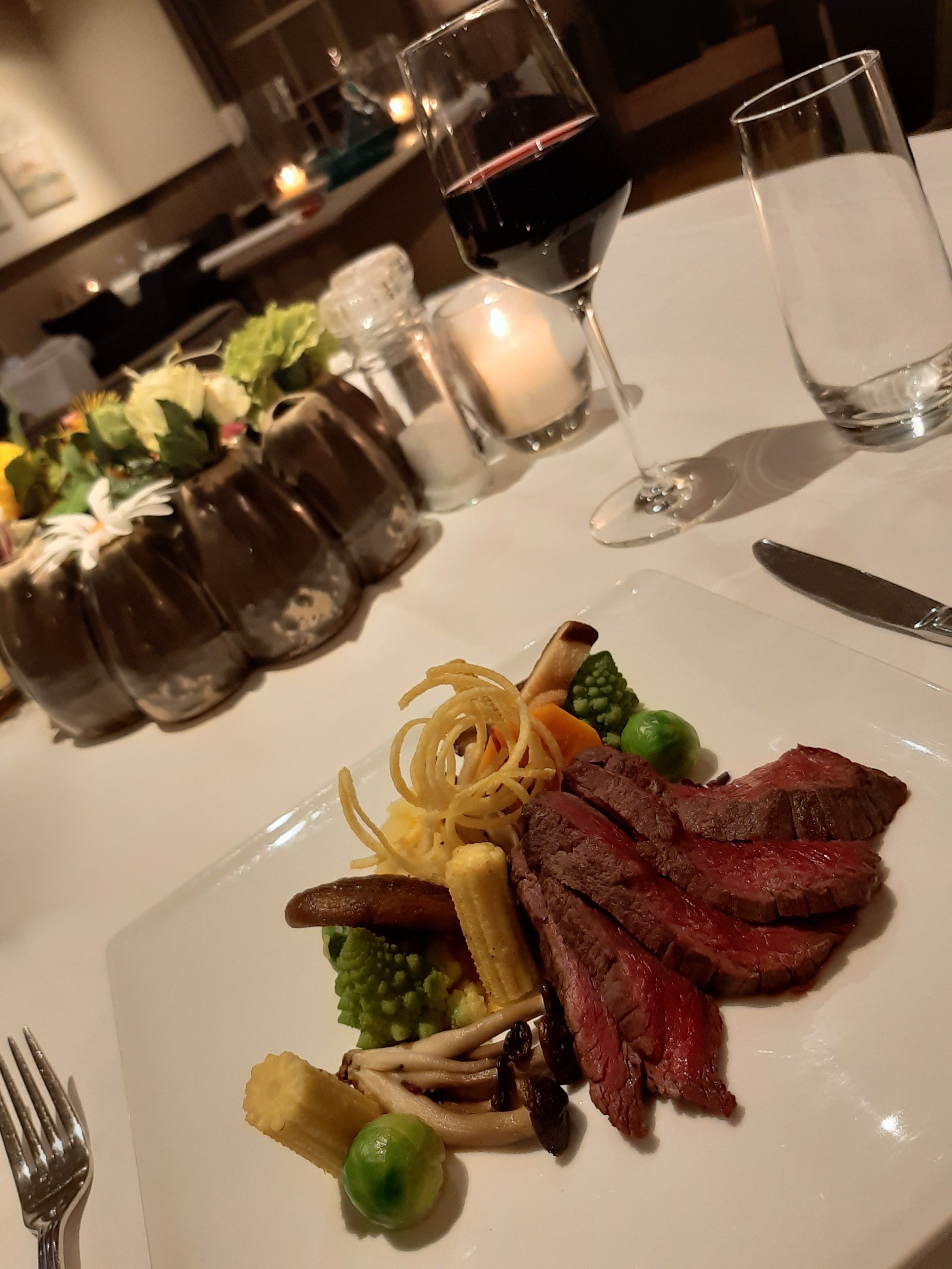 Una mesa de comedor con un plato de comida, una copa de vino y saleros y pimenteros.