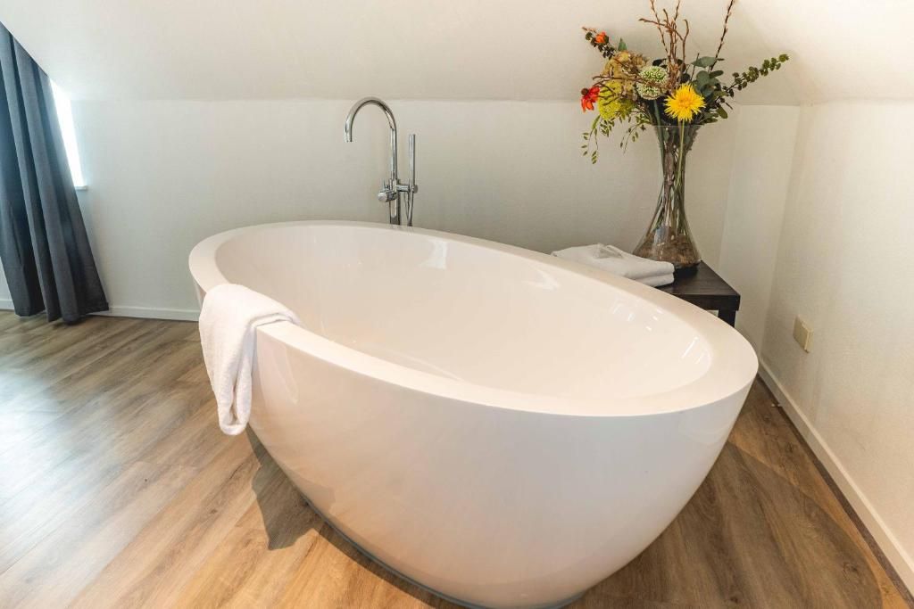 Un baño moderno con una bañera independiente, ducha y un florero con flores sobre una mesita.