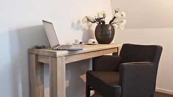 Ein Laptop steht auf einem Holztisch, daneben eine Vase mit weißen Blumen und zwei Tassen.