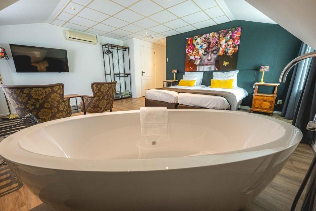 A bedroom with a large bathtub, a bed with two pillows, a TV, and a painting on the wall.