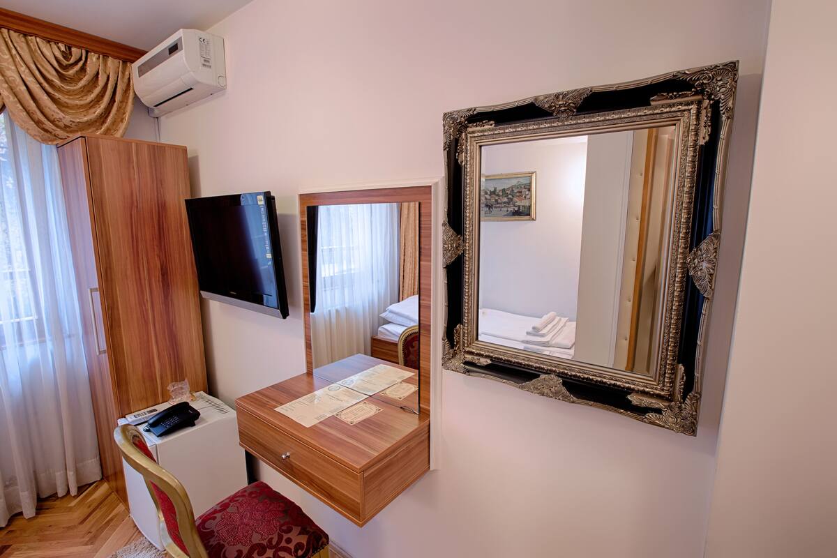 A hotel room with a wooden desk, a flat-screen TV, a large ornate mirror, and a wardrobe.