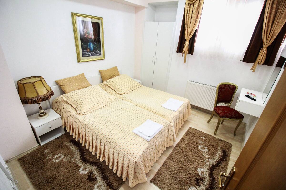 A bedroom with two beds, a nightstand, a chair, a desk, and a radiator.