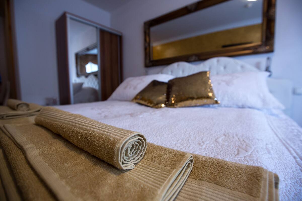 A neatly made bed with rolled towels, a mirror, and decorative pillows.