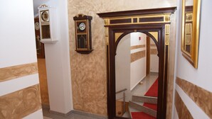 A hallway with a wooden-framed mirror, a clock, and a staircase with red steps. - Hotel Herc (Sarajevo)