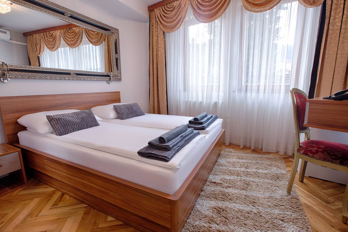 A double bed with a wooden headboard, a bedside table, a chair, and a large mirror.
