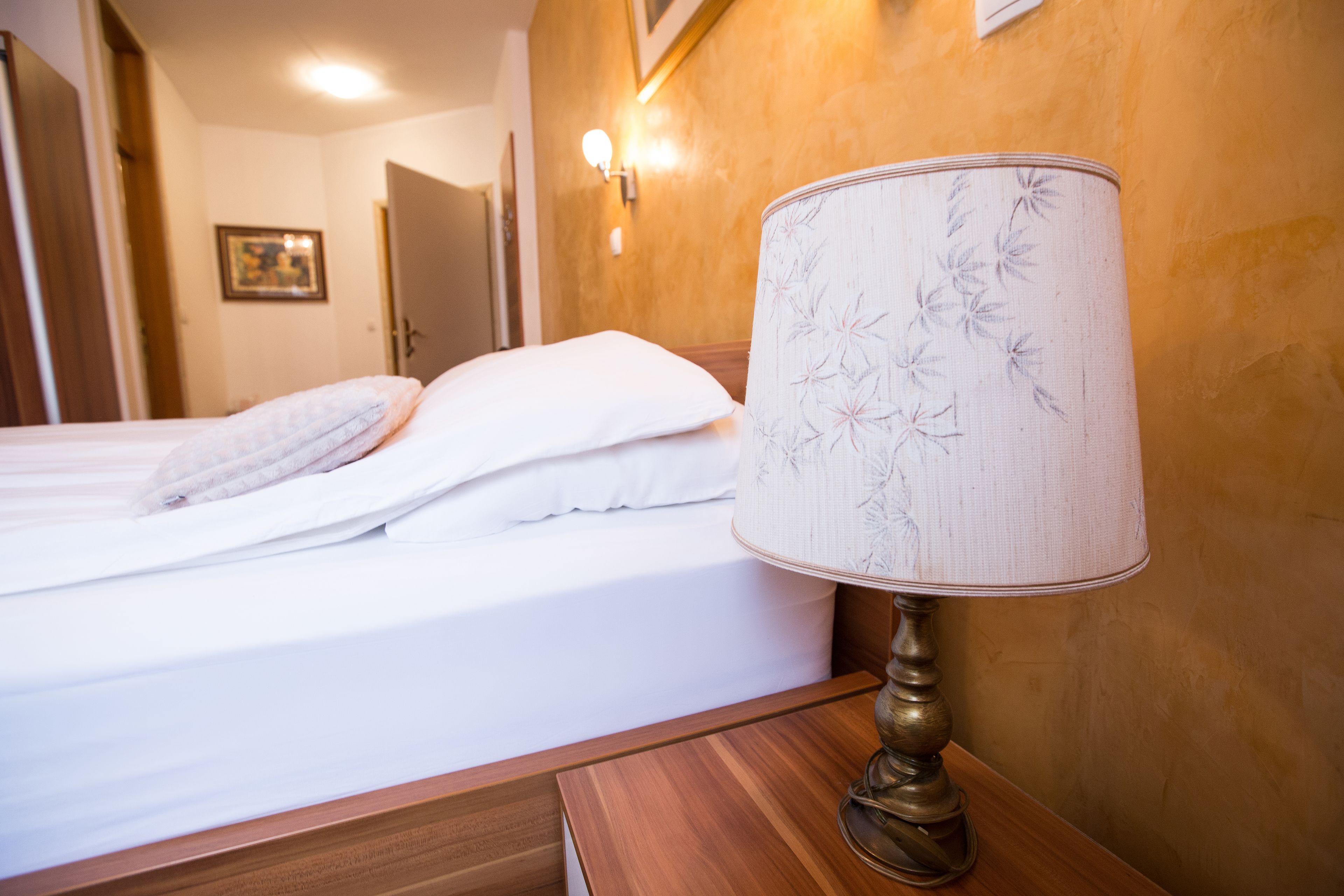 A neatly made bed with white linens and a decorative lamp on a wooden nightstand.