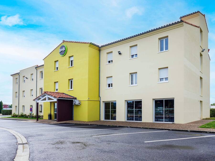 A two-story hotel with a yellow and beige facade, a covered entrance, and a parking lot.
