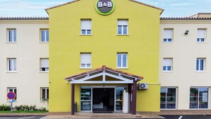 A yellow building with a B&B sign, a covered entrance, and a no parking sign. - B&B HOTEL Agen Castelculier (Castelculier)