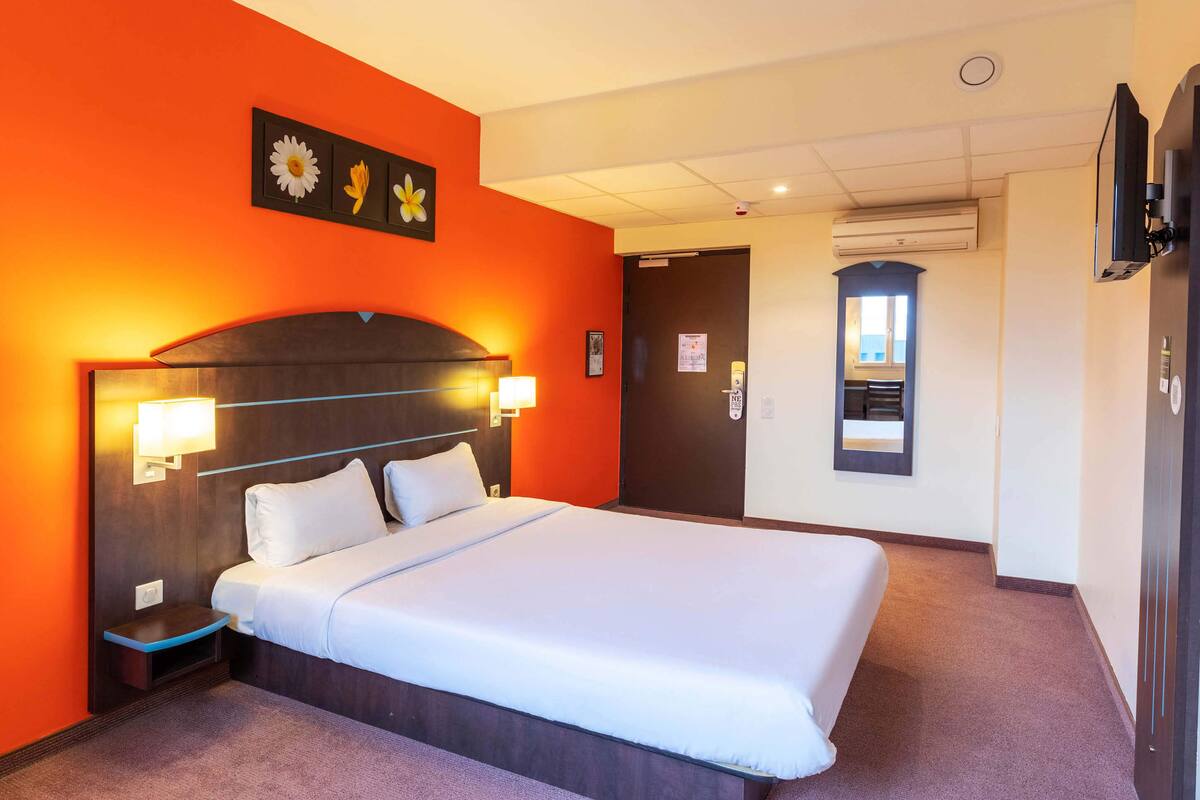 A hotel room with a large bed, a nightstand, a wall-mounted TV, and a door leading to a bathroom.