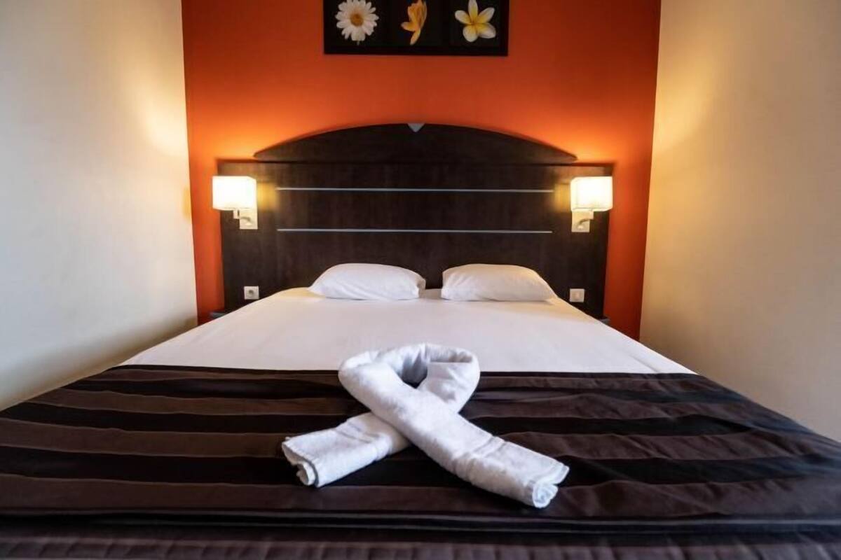 A hotel room with a bed, two bedside lamps, and a towel on the bed.