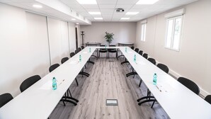 A conference room with a long table, chairs, and a projector screen. - B&B HOTEL Agen Castelculier (Castelculier)