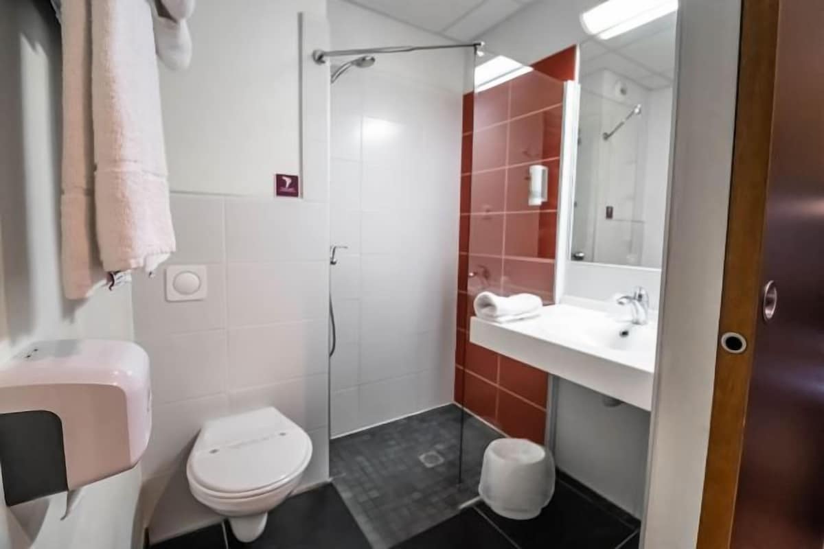 A bathroom with a toilet, sink, shower, and mirror.