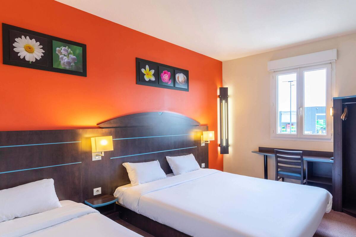 A hotel room with two beds, a desk, and a window.