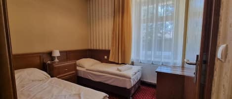 Habitación de hotel con dos camas, un escritorio, una lámpara y una ventana con cortinas.