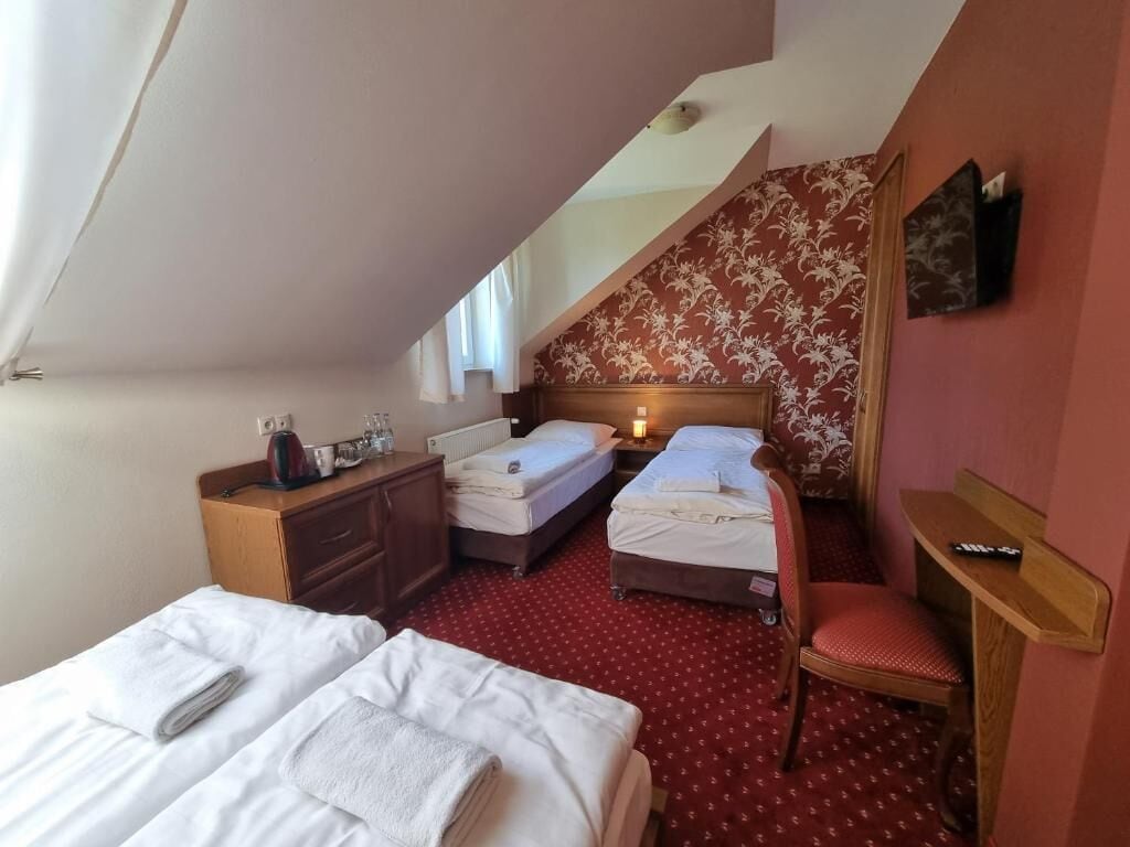 A room with two beds, a desk, a chair, and a small table with a remote control.