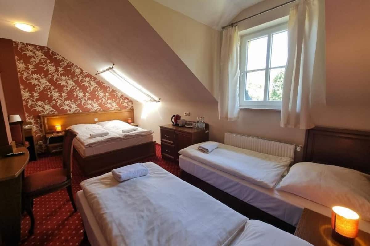 Ein Hotelzimmer mit zwei Betten, einem Schreibtisch, einem Stuhl, einem Heizkörper, einem Fenster mit Vorhängen und einer Lampe.