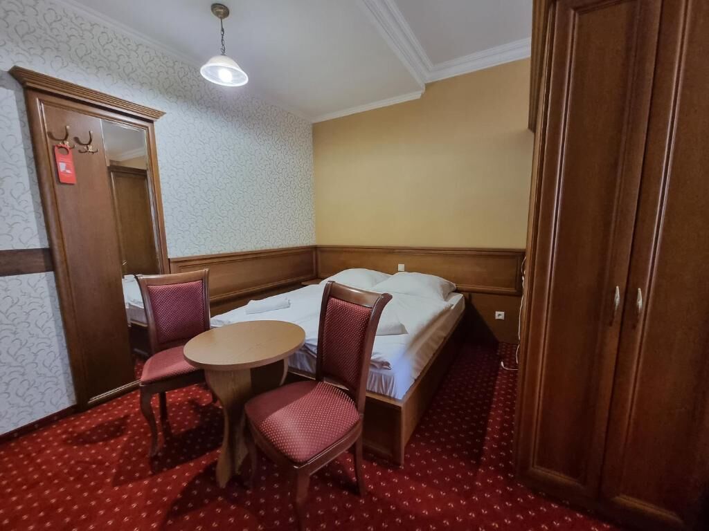 A hotel room with a bed, a small round table, two chairs, a wardrobe, and a mirror.