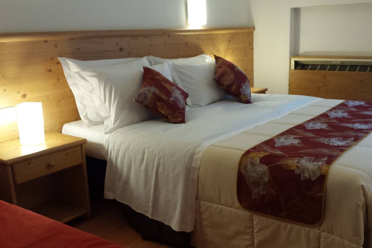 A neatly made bed with a floral throw blanket, white bedding, and two decorative pillows.