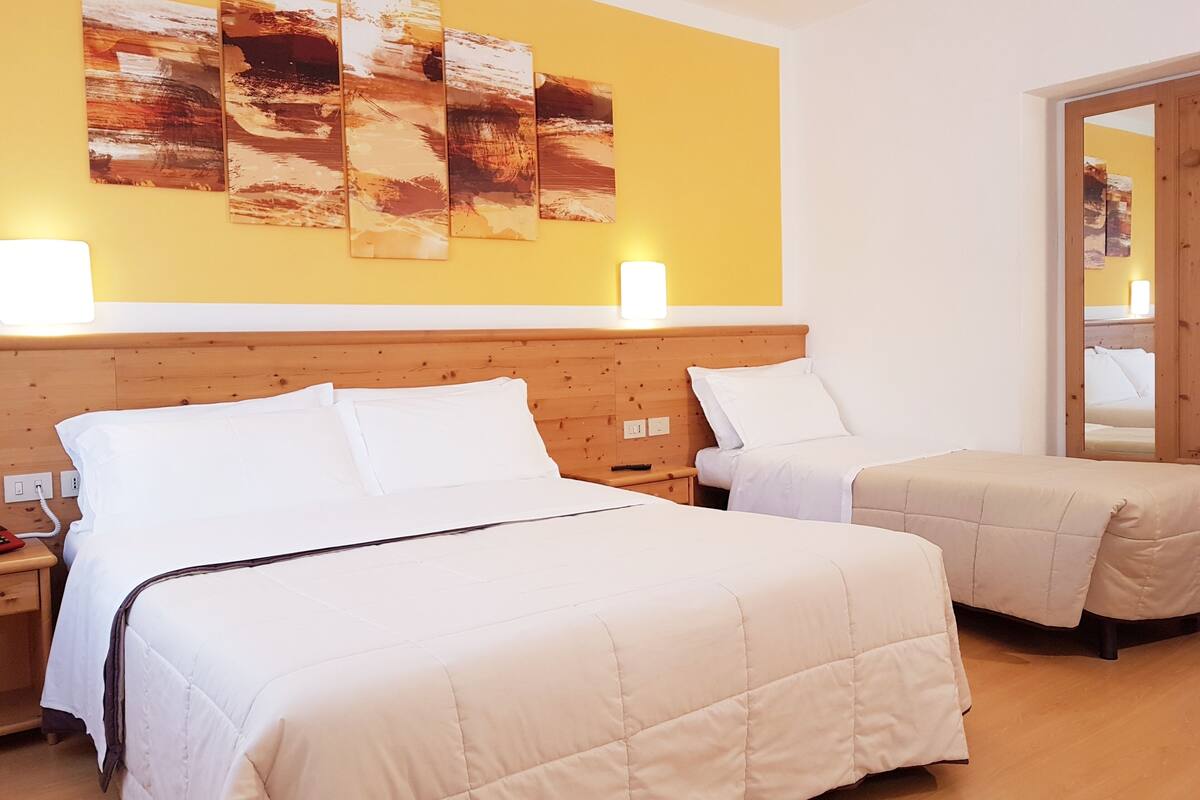 A hotel room with two beds, a wooden headboard, and a yellow wall with abstract art.